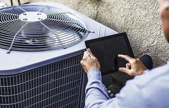 HVAC technician using digital tablet to inspect air conditioning unit